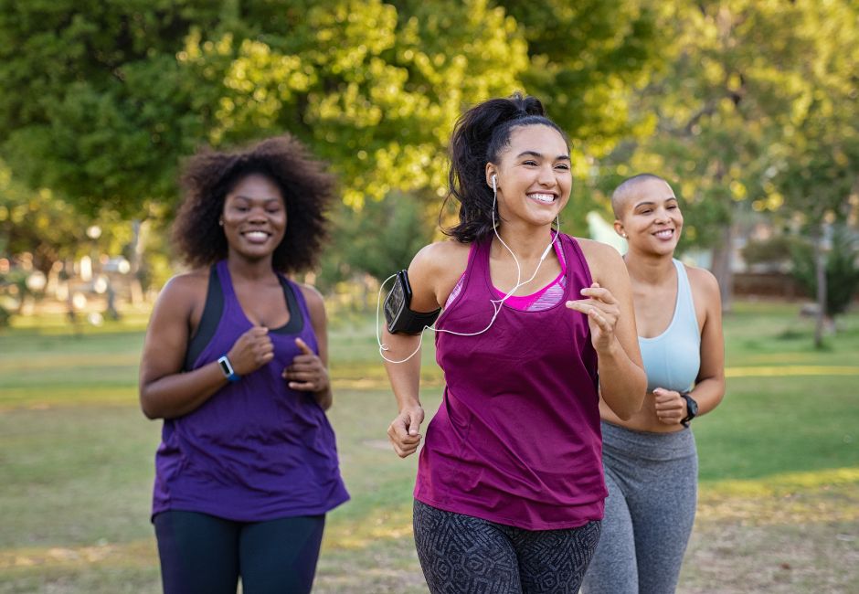 Three women jogging together in a park, smiling and enjoying outdoor exercise as part of a sustainable weight loss journey.