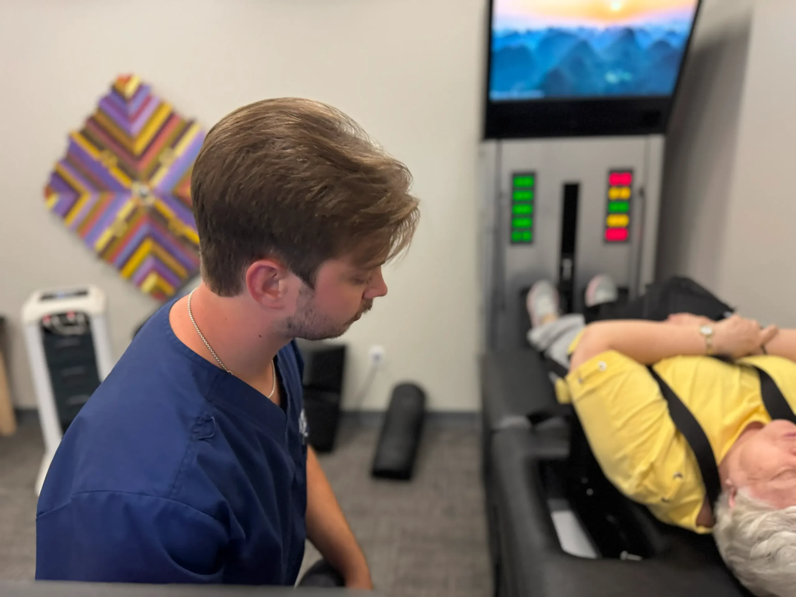 Healthcare practitioner adjusting an older patient lying on a therapy or rehabilitation machine with a screen in the background.